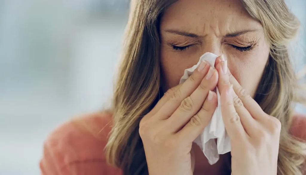Sneezing can be a sign of CPAP lung infection. A headshot of a woman sneezing with a tissue in her hands covering her nose.